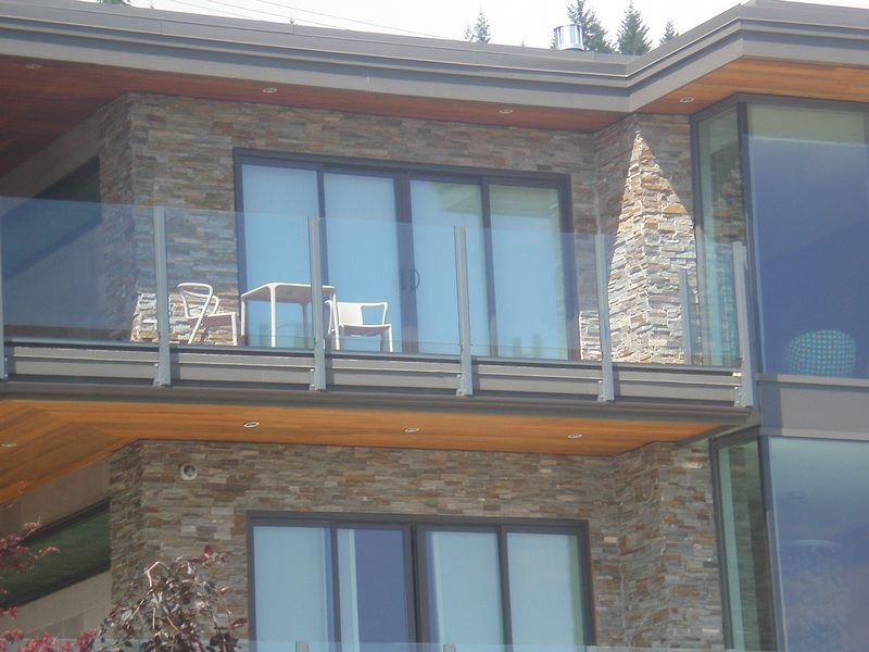 Glass balcony railing with aluminum posts on a stone-clad home